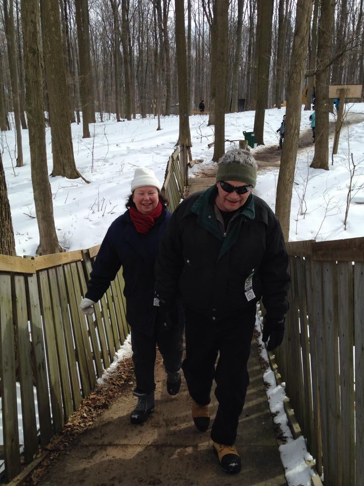 Winter scene of Charmaine and Vic walking over a rocking bridge at White Meadows Maple Syrup farm